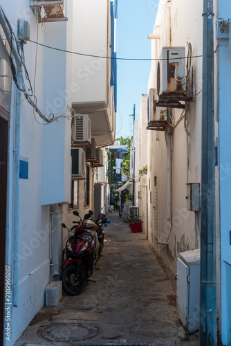 Bodrum, Turkey. Charming narrow street in the old town with whitewashed houses, parked scooters, decorative terracotta pots with green plants, and traditional stone pavement.