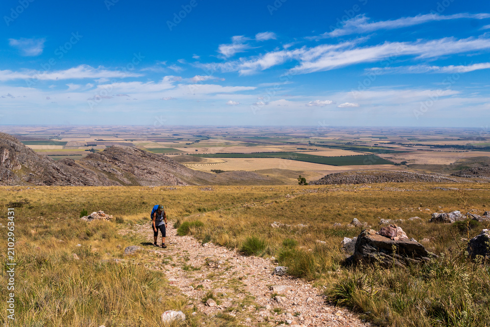 Obraz premium scenic view over farmland and hills and a blue sky from a trail in Sierra de la Ventana with a hiker coming up the trail