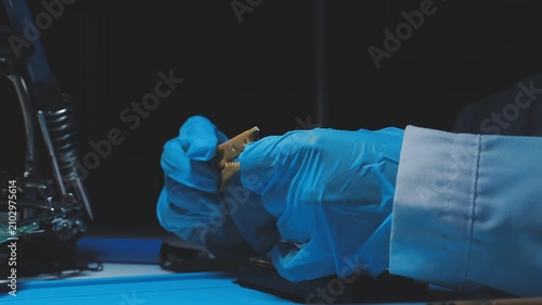 Technician inspecting a circuit board with a magnifying glass. Close up of hands in blue gloves working on microelectronics in a laboratory.