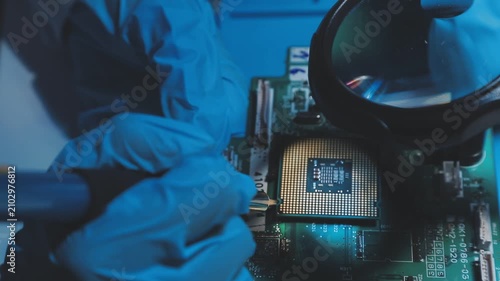 Technician inspecting a circuit board with a magnifying glass. Close up of hands in blue gloves working on microelectronics in a laboratory.