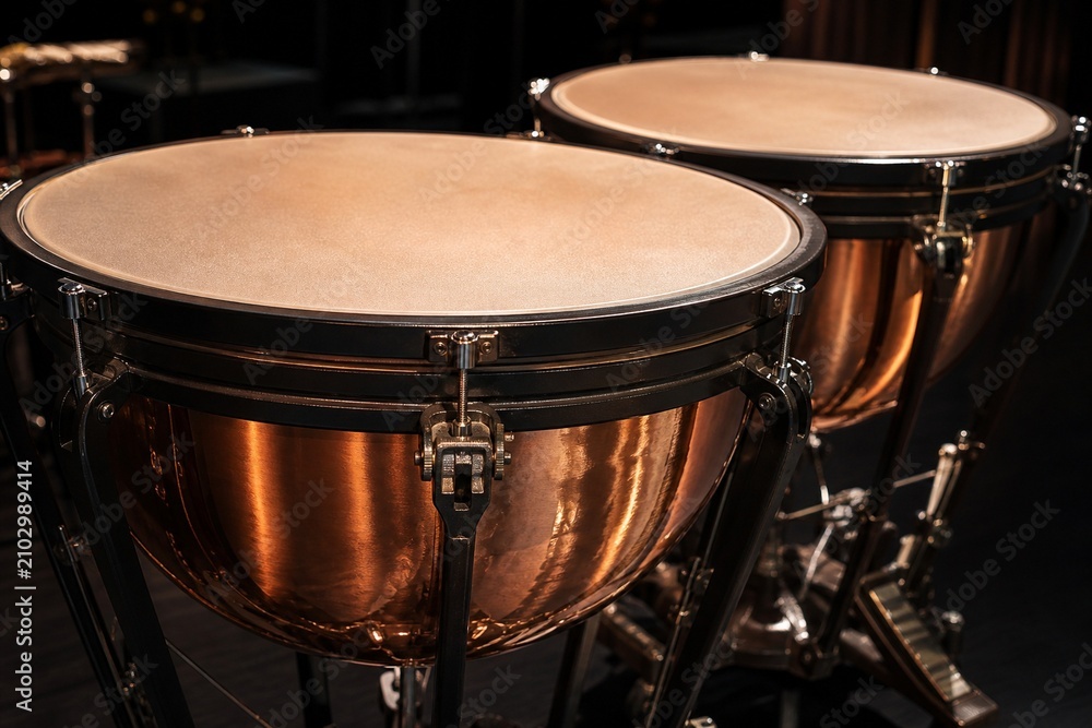 Fototapeta premium A pair of polished copper kettledrums with taut drumheads gleaming under focused stage lighting.