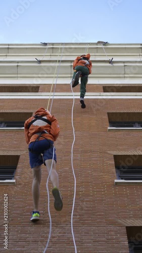 Two Charity Fundraisers Abseiling Down a High-Rise Brick Building Side by Side.