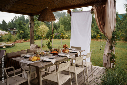Konstfotografi An outdoor dining setup on a wooden table under a gazebo in a lush green garden