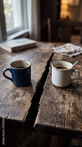 Two coffee cups on a rustic wooden table, contrasting colors, one blue and one white, soft natural light reflecting warmth