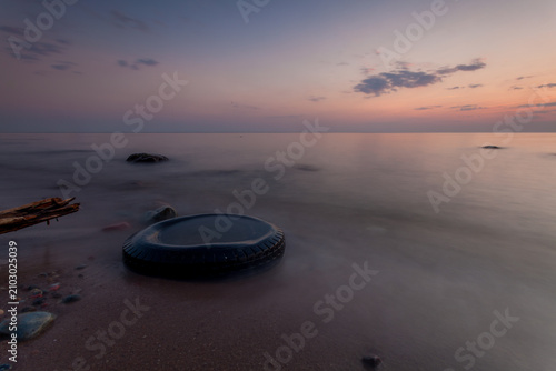 Discarded tire on beach at sunset