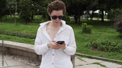 woman in light clothing reads a smartphone in a city plaza, representing electronic health records, telemedicine access and confidence after treatment during an independent city walk
