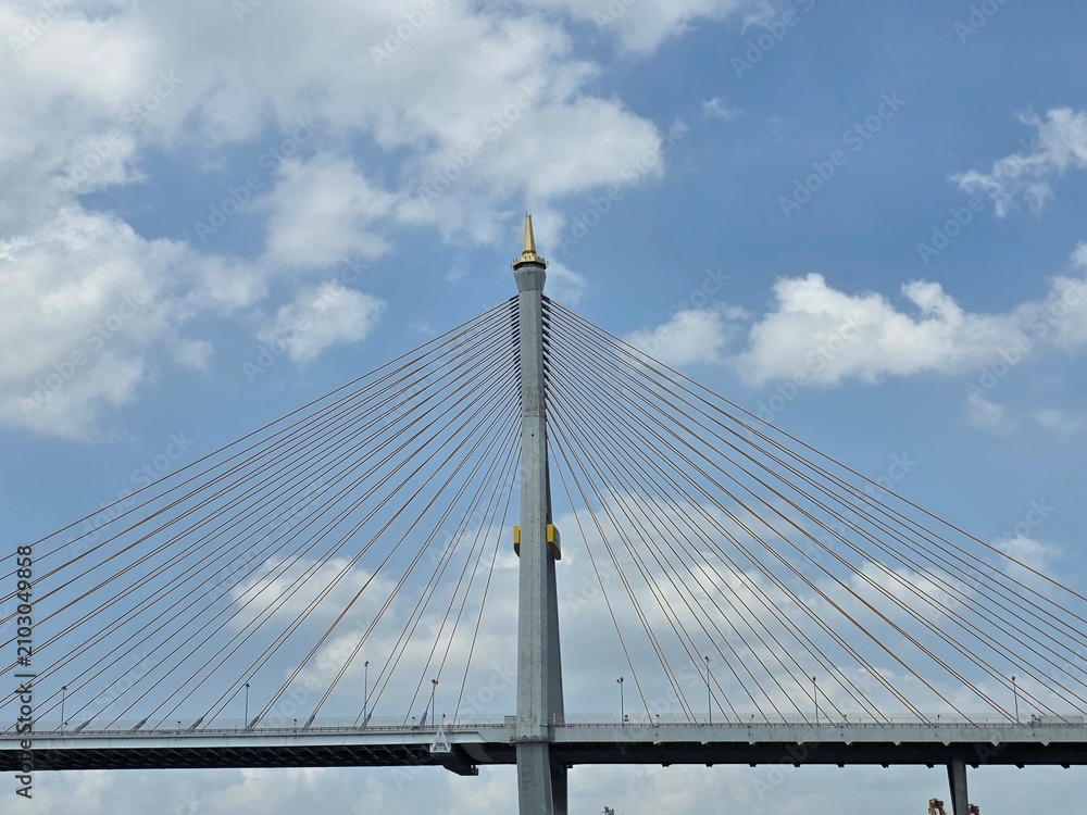 Obraz premium Modern Cable-Stayed Bridge Tower: A majestic tower of a cable-stayed bridge reaching towards a partly cloudy blue sky, showcasing intricate engineering and architectural design.