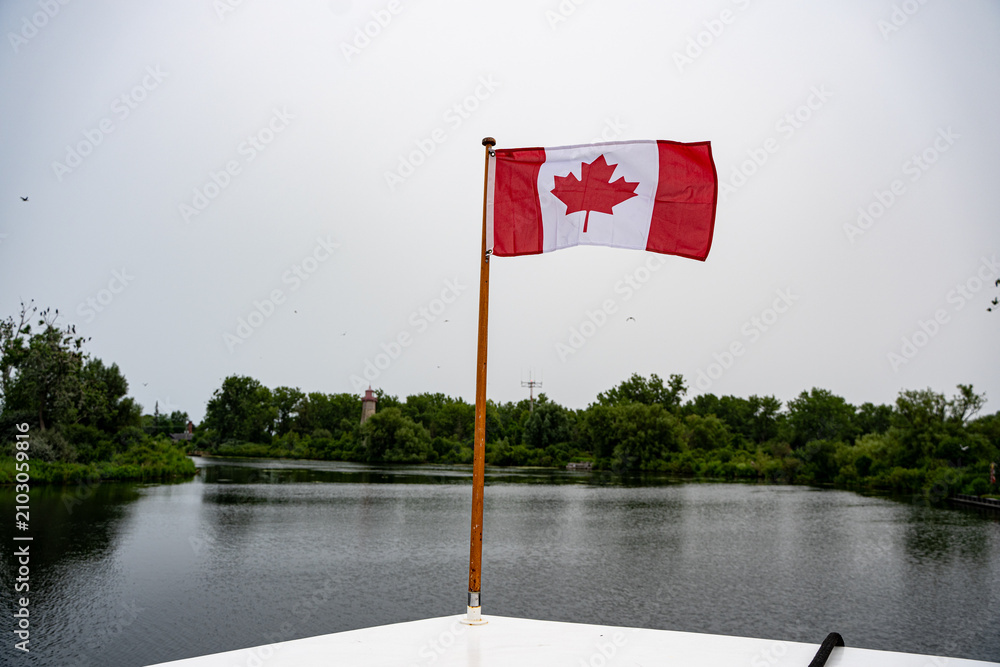 Fototapeta premium Canadian flag flying above calm island waterway.