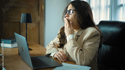 Εκτύπωση καμβά Young Hispanic businesswoman yawning while working in her office, showing fatigue and tiredness during a long workday in a modern professional workplace