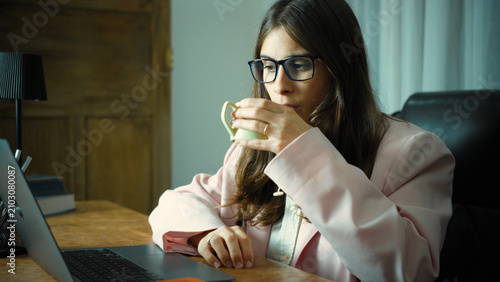 Bild auf Leinwand Young Hispanic businesswoman in her office drinking a cup of coffee, taking a brief moment to relax during her workday in a modern professional workplace