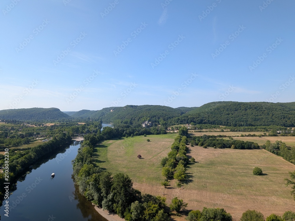 Obraz premium High-angle panoramic view of the Dordogne River winding through a lush green valley with distant hills in Beynac-et-Cazenac, France