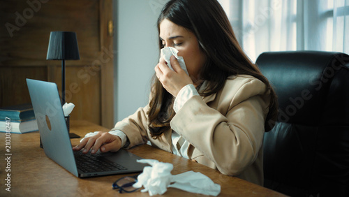 Foto Young Hispanic businesswoman working in her office while suffering from severe nasal congestion and feeling unwell, trying to stay productive despite her physical discomfort