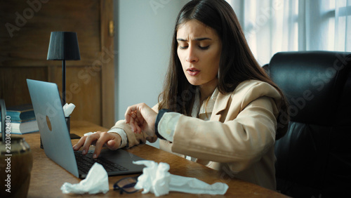 Foto Tired young Hispanic businesswoman in her office looking at her wristwatch, eagerly waiting for the end of her workday after a long and exhausting day at work