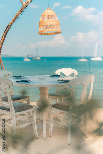 Romantic beach outdoor dining table umbrella parasol ocean view sand shore coast vertical summer scene. Romantic travel vacation holiday couples honeymoon lifestyle getaway background wallpaper design
