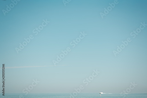 Bild auf Leinwand A distant boat moves across calm blue water beneath a wide, cloudless sky with extensive copy space