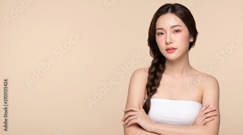 young woman with long dark braided hairstyle, natural makeup, standing with crossed arms, with a confident expression, isolated on a beige seamless studio background