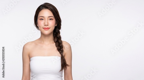 young woman with long dark braided hairstyle, natural makeup, wearing a white strapless tube top, walking confidently, with a confident expression, isolated on a white seamless studio background