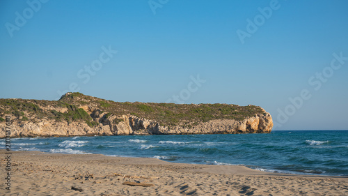 Cuadro en lienzo Wide view of a sandy beach and rolling waves with a prominent rocky cliff headla