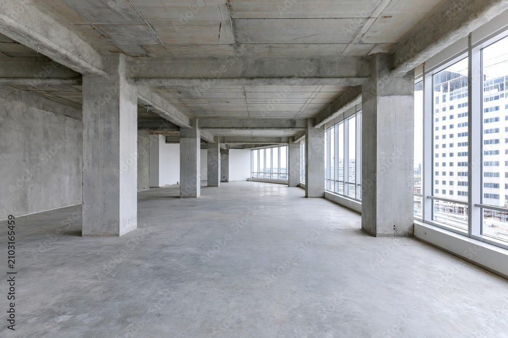 Obraz premium The Empty Concrete Interior with Expansive Windows and Pillars Along Bright Open Space