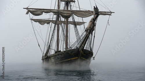 Ghost ship drifting through sea mist with tattered sails, eerie maritime scene
