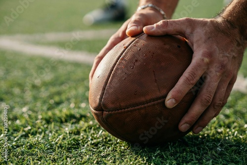 Close Up of American Football Player Hands Placing Leather Ball on Green Grass Turf Field for Kickoff, Sports Competition Concept with Selective Focus and Natural Sunlight Outdoor Background