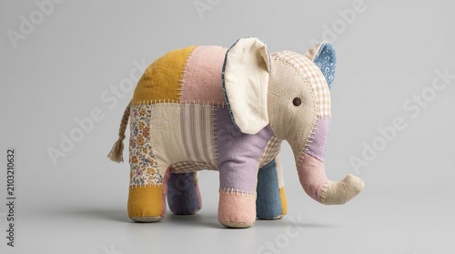 A close up studio shot of a beautiful, brightly colored, handmade, soft toy elephant on a plain light gray background, facing right.