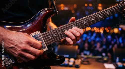 Musician playing electric guitar on stage during live concert performance at music festival with professional lighting and blurry audience background in dark club.