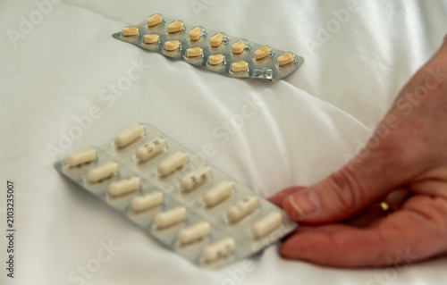 фотографія Pill packets on a white bedcover with a hand reaching