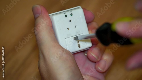 Close-up of hands using a screwdriver to unscrew a small electronic device to reveal internal battery.