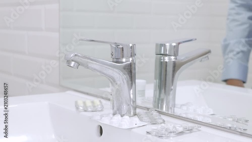Blurred Shooting with a Sick and Nervous Person in Bathroom Looking in the Mirror with Many Medical Pills on the Sink.