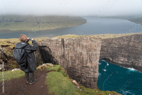 Young Adult Woman Photographing Sorvagsvatn Lake and Ocean View from Traelanipa Cliffs, Faroe Islands