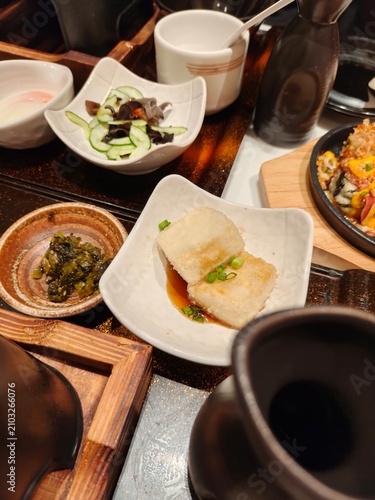 Japanese side dishes set featuring agedashi tofu, cucumber salad, and pickles on wooden table