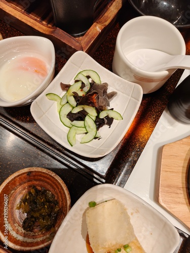 Japanese side dishes set featuring agedashi tofu, cucumber salad, and pickles on wooden table