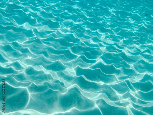 Turquoise sea water ripples background for summer vacation travel banner design. Clear ocean ripple wave surface texture for tropical resort promotion, swimming pool poster, and cosmetic mockup templa