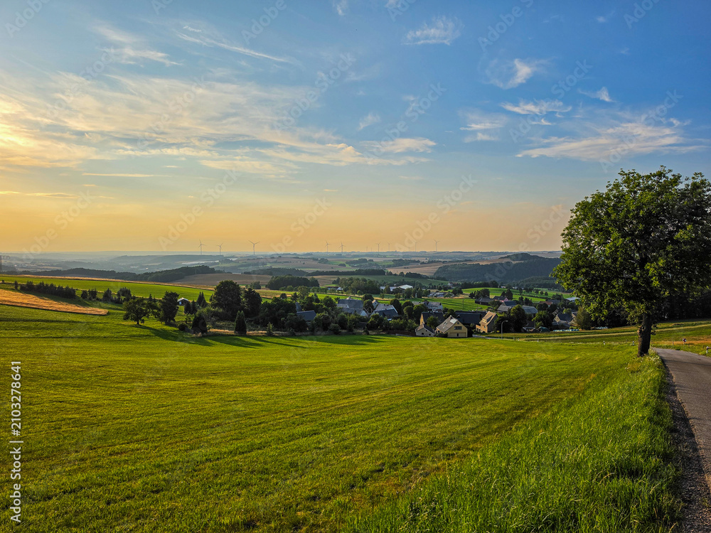 Obraz premium rolling green countryside with village at golden sunset under a colorful evening sky