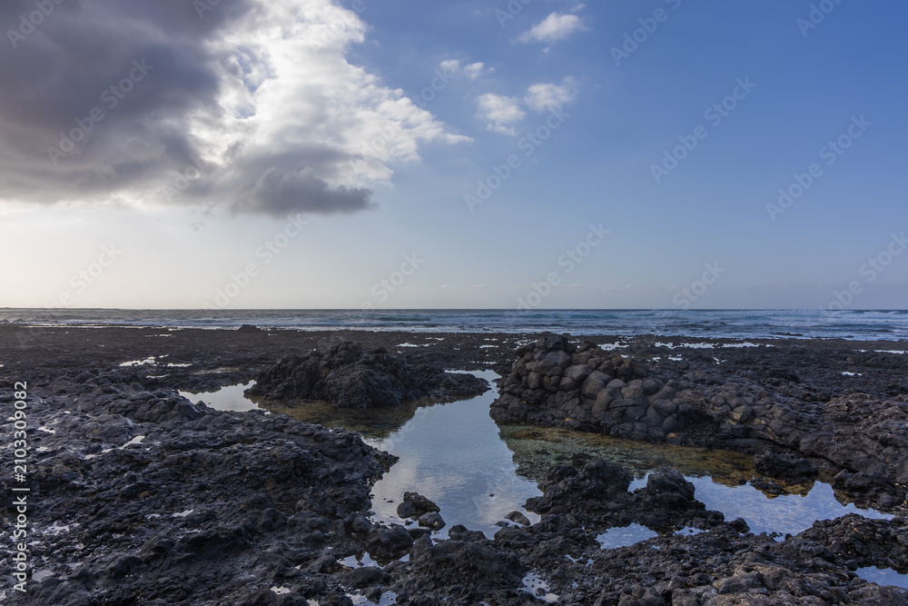 Fototapeta premium Dramatic dark storm clouds contrasting with bright sky over volcanic coast pools