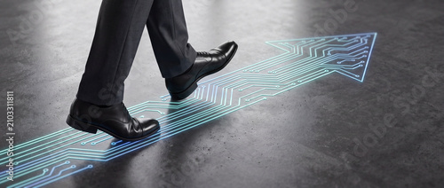 Businessman stepping on digital circuit path illuminated by glowing blue neon light on a dark concrete floor, representing corporate innovation, career growth, and technological progress