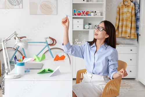 Young Asian businesswoman with paper plane at home
