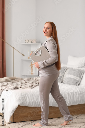 Young overweight woman with scales in bedroom