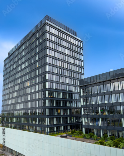 Modern office building in a city. A view of a tall office building with glass windows located in a bustling city center during daytime.