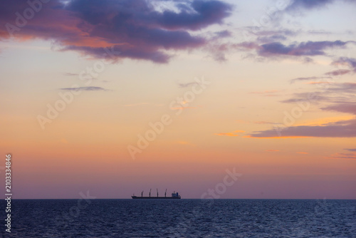 Cargo Ship Sailing on Ocean at Sunset