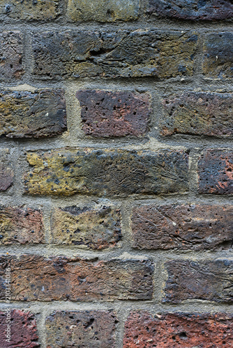 Aged and weathered multi colored rough texture brick wall background with dirt and grim