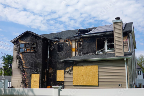 Back view of an abandoned fire damaged house with boarded windows and and doors in suburban setting