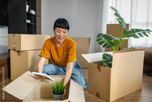 Fotografie Japanese woman packing houseplants and boxes while smiling during a home move