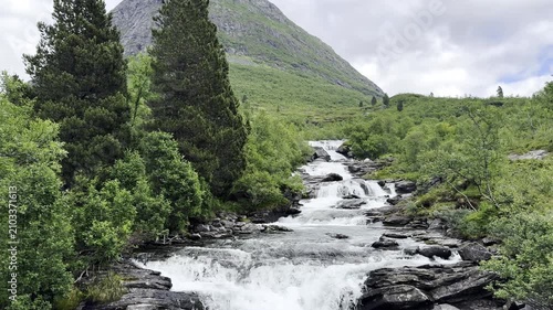 Crystal-clear water cascades down steep mountain slopes, forming beautiful waterfalls among rugged rocks and pristine Norwegian nature. Spectacular Scandinavian landscape with flowing water, dramatic 