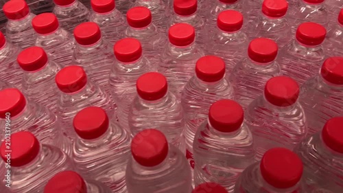 Rows of small plastic water bottles with blue and red caps displayed on store shelves. Close-up of packaged bottled drinking water in a retail supermarket beverage section