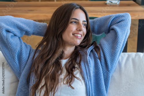 Foto Young woman relaxing on a couch at home, smiling and comfortable in a cozy blue