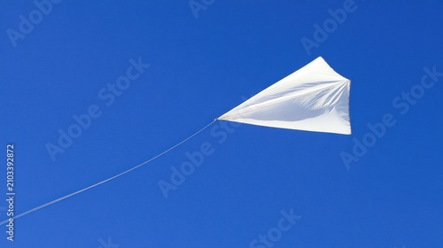 White kite flying high in a clear blue sky