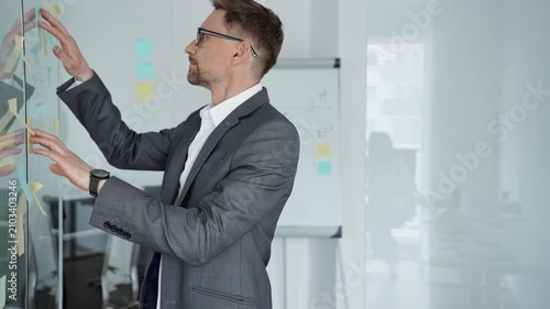Business professional deeply contemplating project strategy, analyzing ideas and planning solutions on a glass wall with sticky notes in a modern office environment