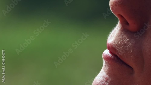 Close-up of a person exhaling a visible plume of vapor or steam. A detailed profile view captures the moment of exhalation, showing vapor dissipating into the air with a blurred green background
